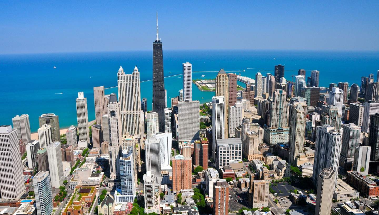 Willis Tower Aerial view of a city with numerous tall buildings near a large body of water under a clear blue sky.
