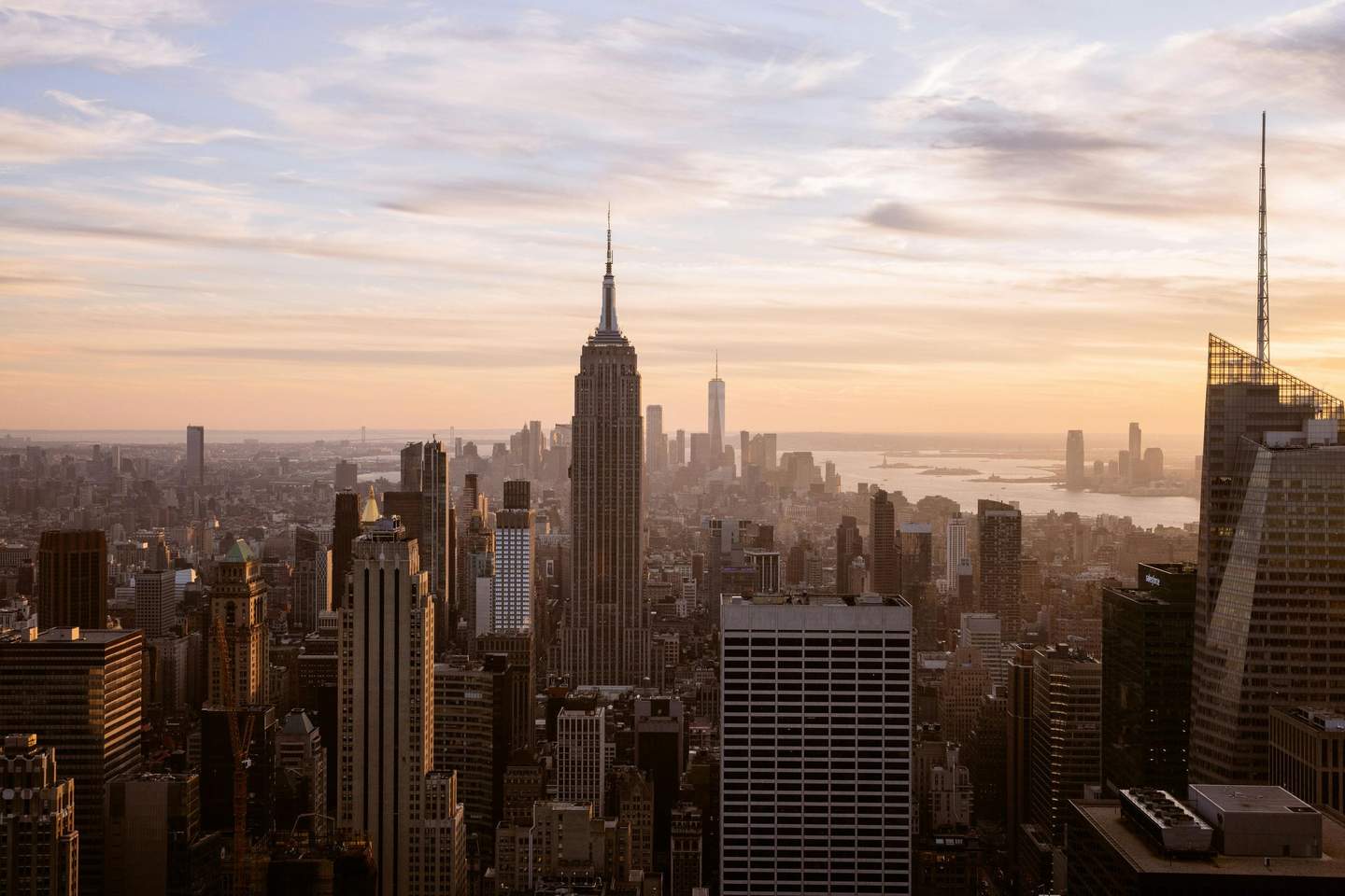 Top of the Rock View of a city skyline at sunset, dominated by tall skyscrapers, with a river and distant buildings in the background.