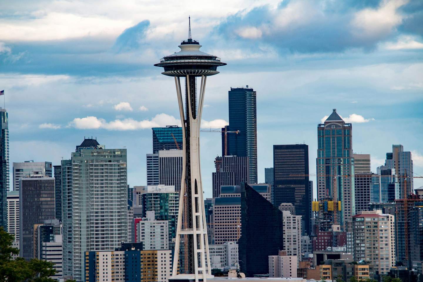 Space Needle A skyline view of Seattle featuring the Space Needle, with a backdrop of various modern skyscrapers under a partly cloudy sky.