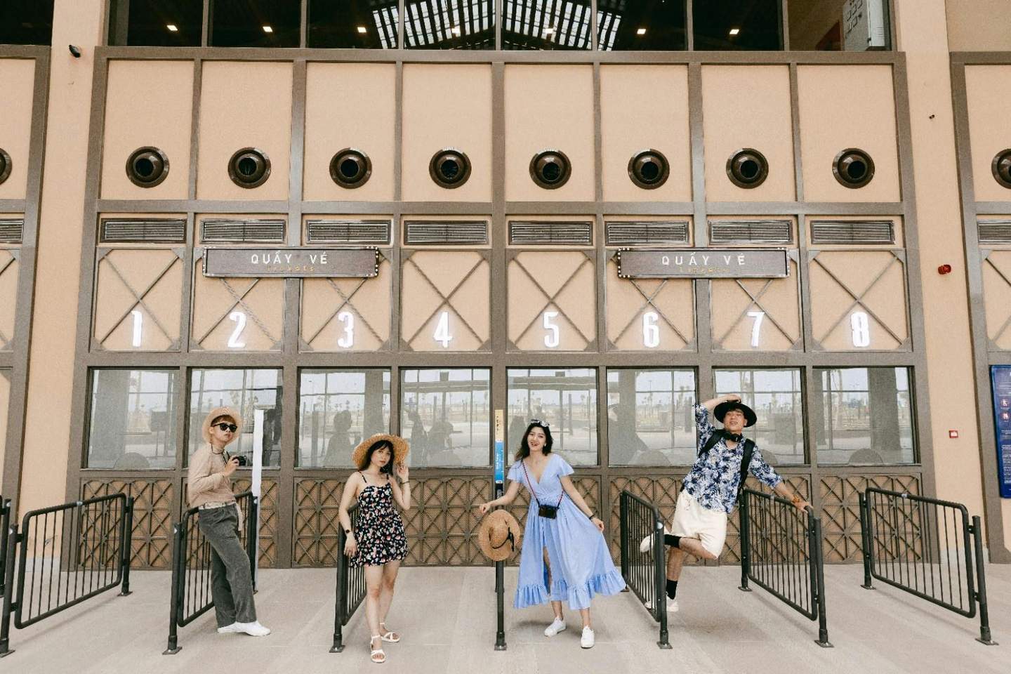 Four people posing in front of a ticket booth with numbered windows and the sign "Quay Ve."