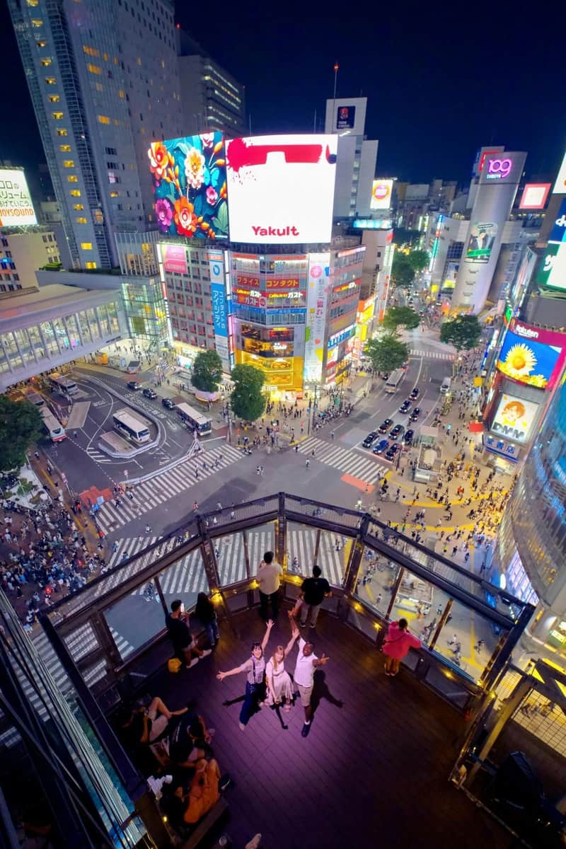 MAGNET by SHIBUYA109 :十字路口景观和屋顶休息室MAG8门票(含饮料和照片) 从上方俯瞰夜间繁忙十字路口的充满活力的城市景观,人们在前台的观景台上。