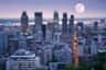 City skyline at dusk with tall buildings and a full moon rising. Lights illuminate the streets and buildings.