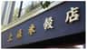 La façade d'un immeuble, sur laquelle se détachent de grands caractères chinois dorés sur un mur sombre, avec des feuilles visibles au-dessus.